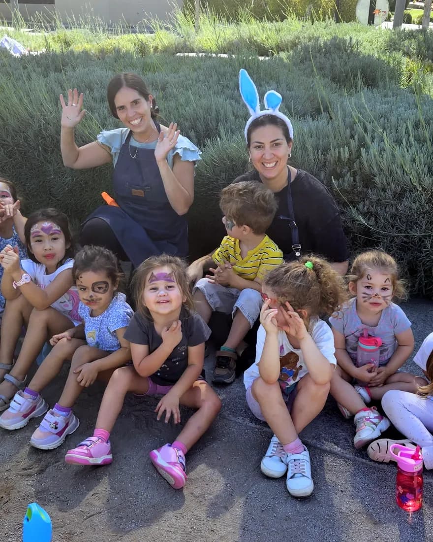 Educadoras y niños con la cara pintada posan sonrientes en un jardín.