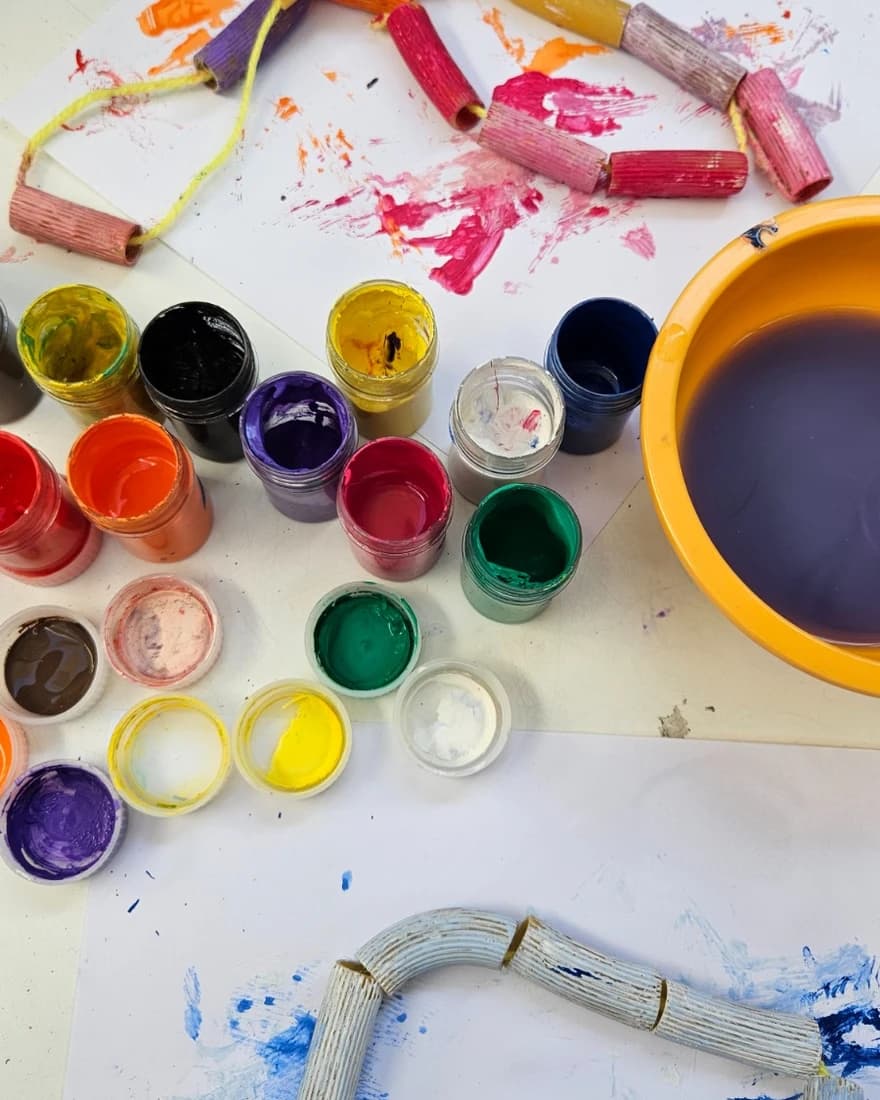 Potes de témpera de colores y collares de tubos pintados por los niños sobre la mesa.
